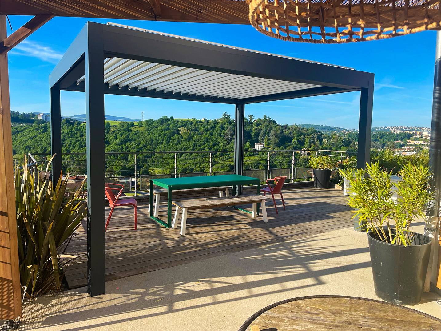 Pergola bioclimatique en aluminium installée sur une terrasse avec vue dégagée sur un paysage verdoyant.