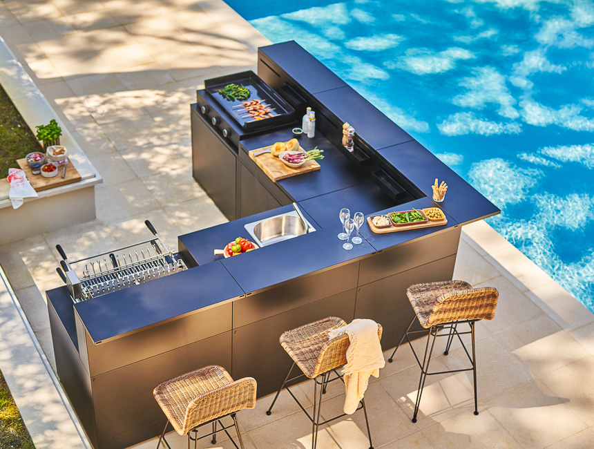 Cuisine extérieure design avec plan de travail et assises, installée en bord de piscine sur une terrasse contemporaine.