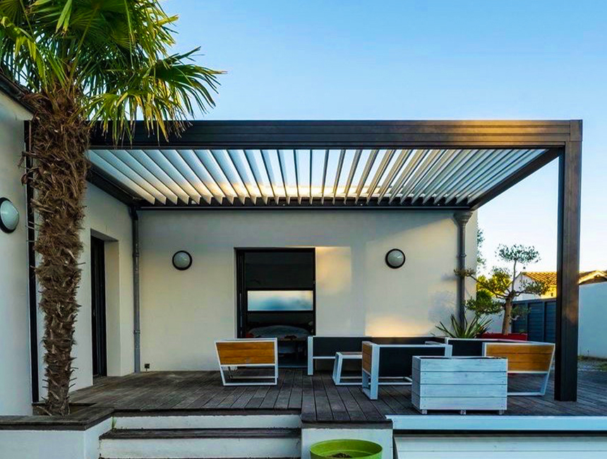 Pergola bioclimatique en aluminium avec lames orientables, installée sur une terrasse en bois attenante à une maison contemporaine.