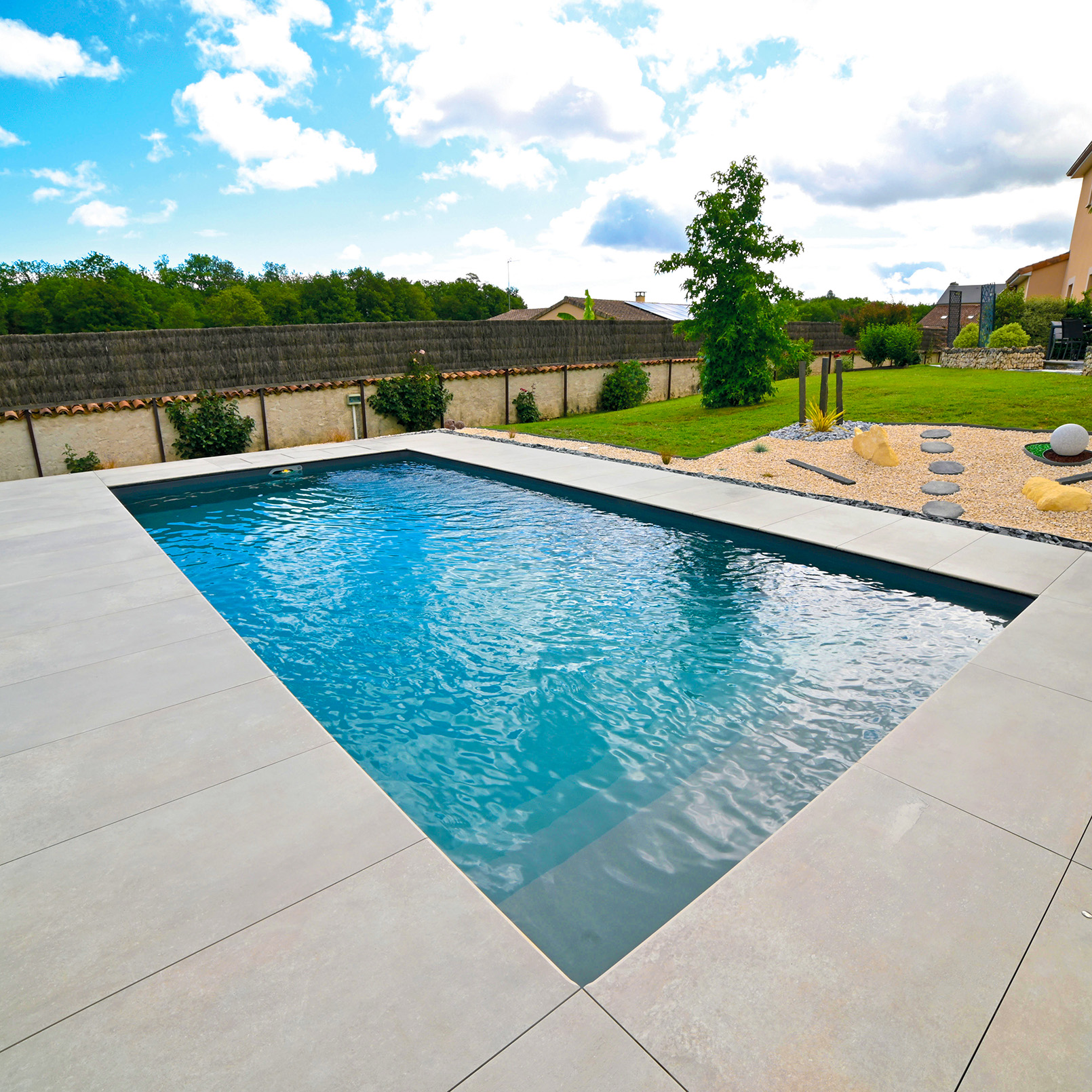 Piscine extérieure contemporaine avec margelles minérales, intégrée dans un jardin paysager.