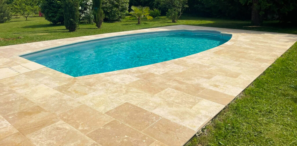 Piscine enterrée aux formes douces avec margelles en pierre naturelle, intégrée dans un jardin arboré.